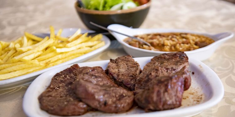 Na carne, uma peça grelhada, tenra e saborosa, acompanhada por arroz de feijão e batatas fritas da casa
